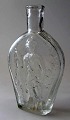 Lomme flaske i 
hvidt glas, 
fastbl&aelig;st 
med figurer i 
relief. 19. 
&aring;rh. 
P&aring; den 
ene ...