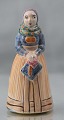 Figur i 
glaseret 
keramik med 
motiv af kvinde 
i lys egnsdragt
Design af L. 
Hjort
Keramik, ...