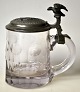 Tysk ølkrus, 1891 i glas med tinlåg. Ælkruset med slibninger. Låg af tin med dekoration af ...