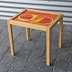 Sidebord i fyrtræ med orange, gult og hvidt dråbemønster under glasplade.Design af ...