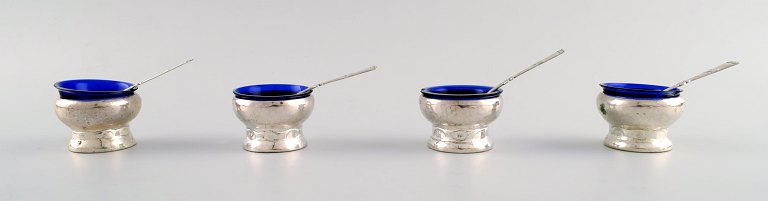 Fernanda Hansen, København. Fire skønvirke saltkar med tilhørende skeer og 
glasindsatser i blåt af tretårnet sølv.